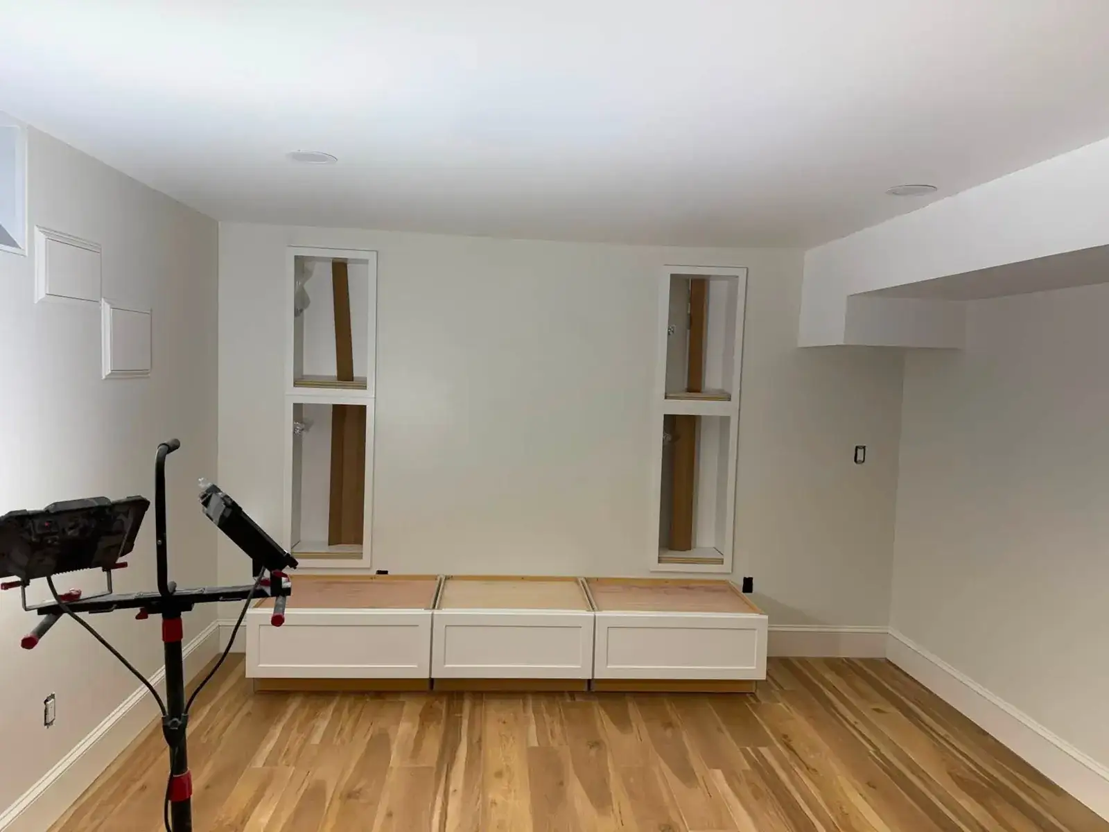 A bright white basement room with new honey-oak plank flooring and a low built-in bench along one wall.